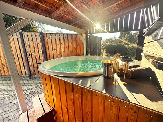 Hotttub met een koeler met fles prosecco en 2 goudkleuige champagne flutes met uitzicht op de wellness tuin door de openslaande luiken
